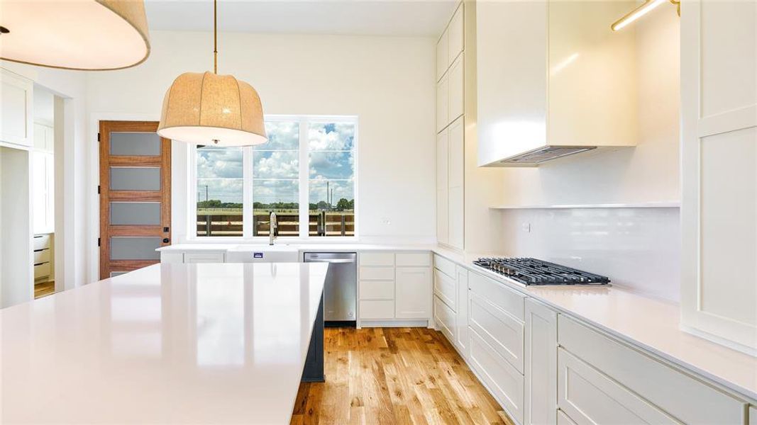 Kitchen with white cabinetry, hanging light fixtures, light wood-type flooring, appliances with stainless steel finishes, and sink