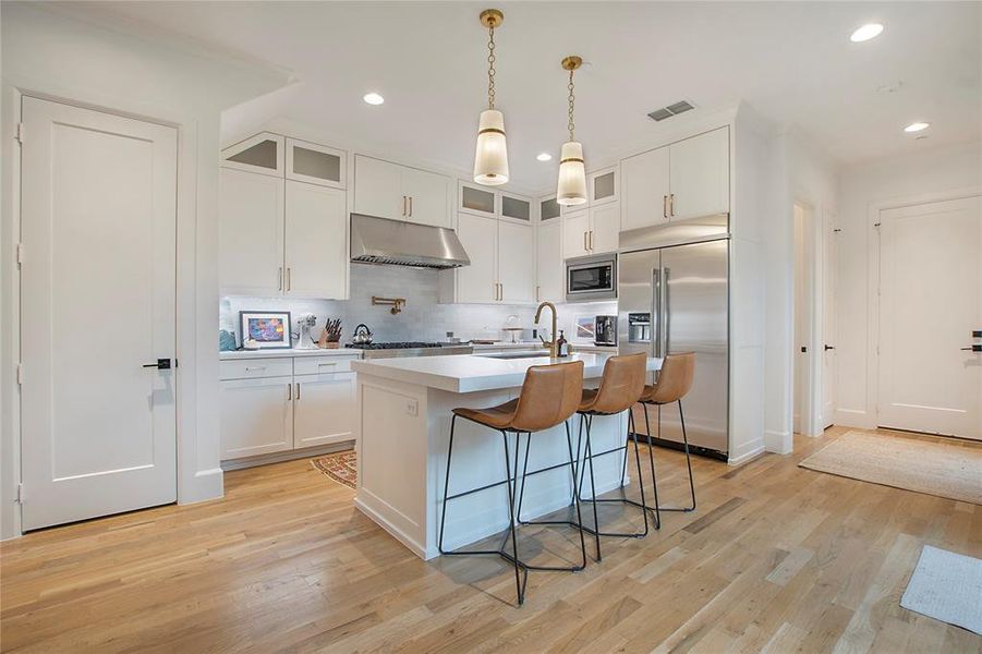 Kitchen featuring white cabinets, a kitchen island with sink, light wood-type flooring, and built in appliances