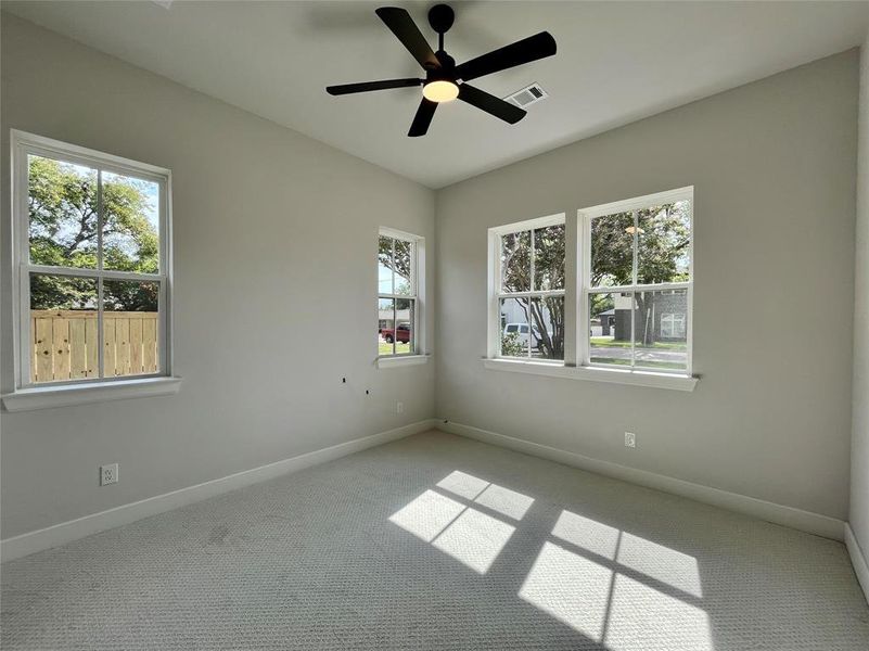 Unfurnished room featuring light carpet, ceiling fan, and a healthy amount of sunlight