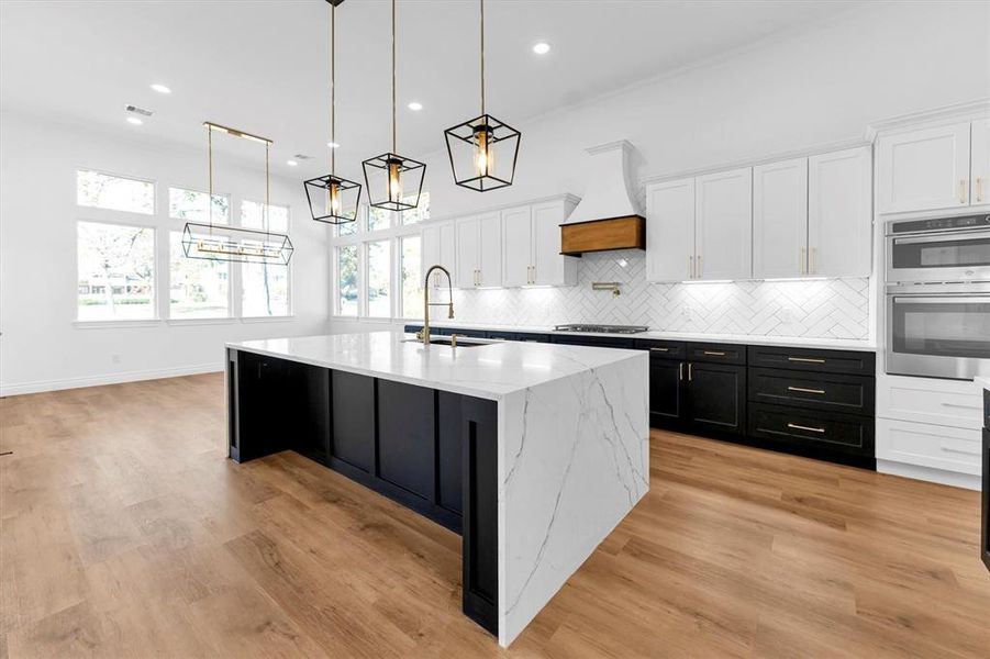 The kitchen island with 9' quartz waterfall countertop, stainless steel sink, black stainless GE dishwasher, and warm brass hardware accented by gold and black pendant lights.