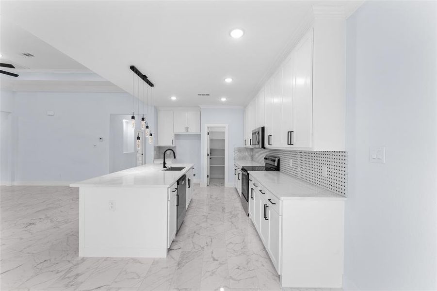 Kitchen featuring white cabinetry, backsplash, stainless steel appliances, and a center island with sink