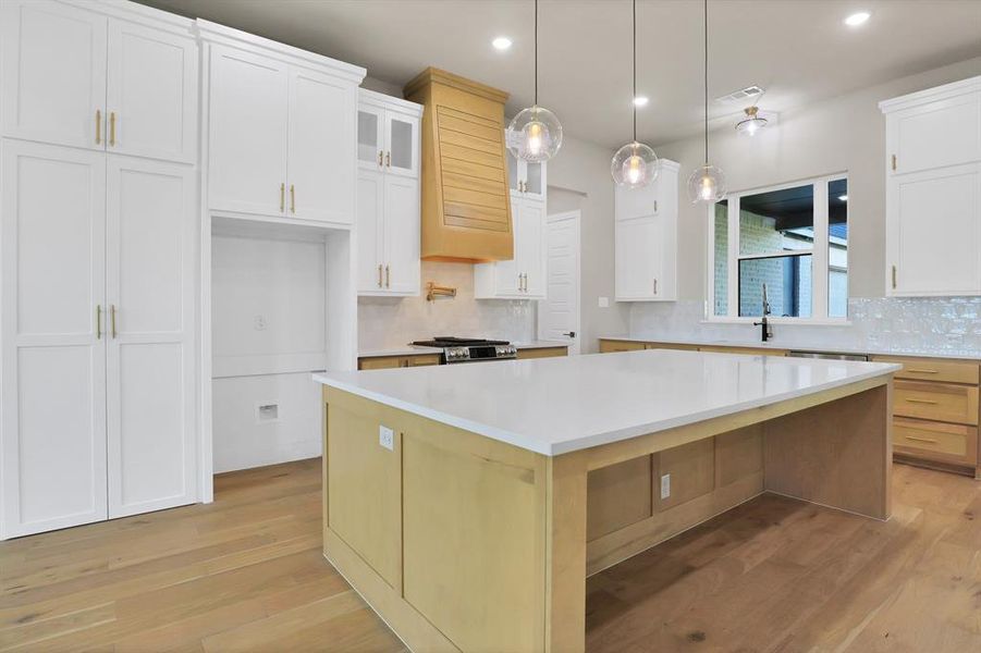 Kitchen with a spacious island, hanging light fixtures, light hardwood / wood-style flooring, and white cabinets