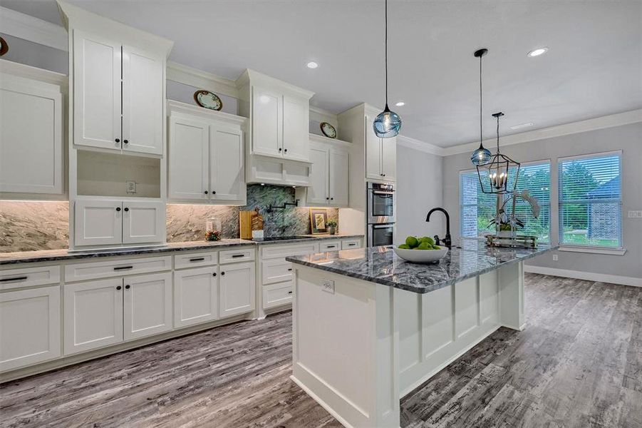 Kitchen with a notable chandelier, white cabinets, and a kitchen island with sink