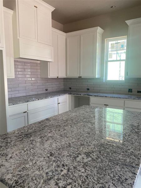 Kitchen featuring white cabinetry, light stone countertops, and decorative backsplash