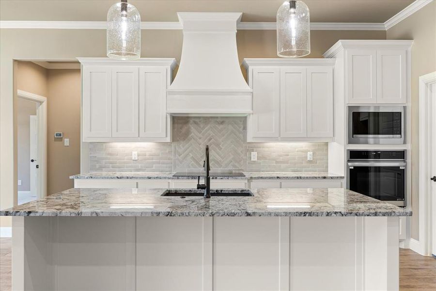 Kitchen featuring custom exhaust hood, appliances with stainless steel finishes, light stone counters, and white cabinets