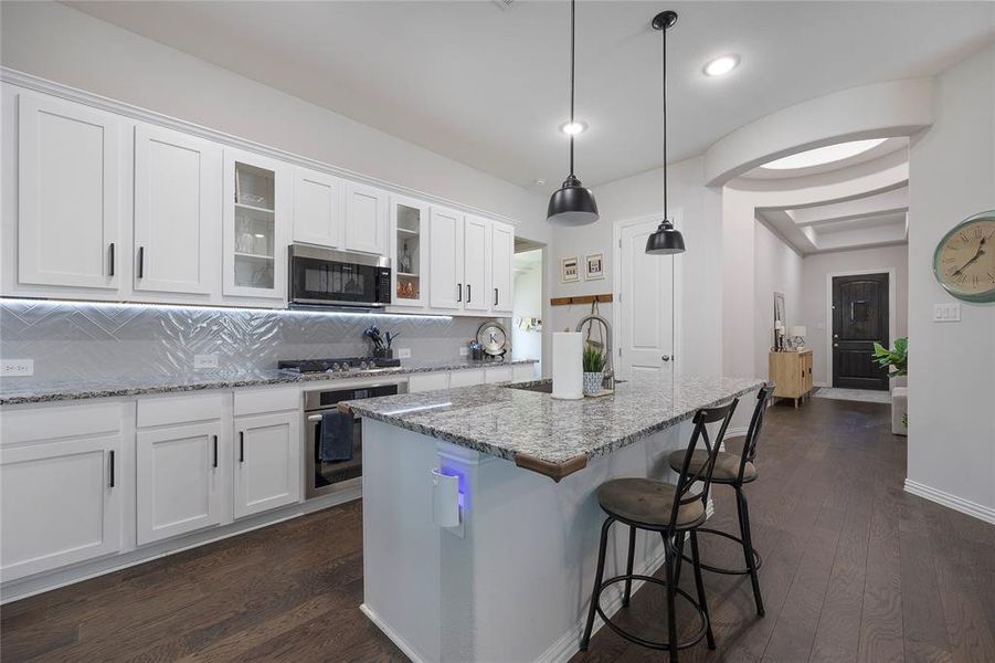 Kitchen with stainless steel appliances, a center island with sink, decorative backsplash, white cabinetry, and dark hardwood / wood-style flooring