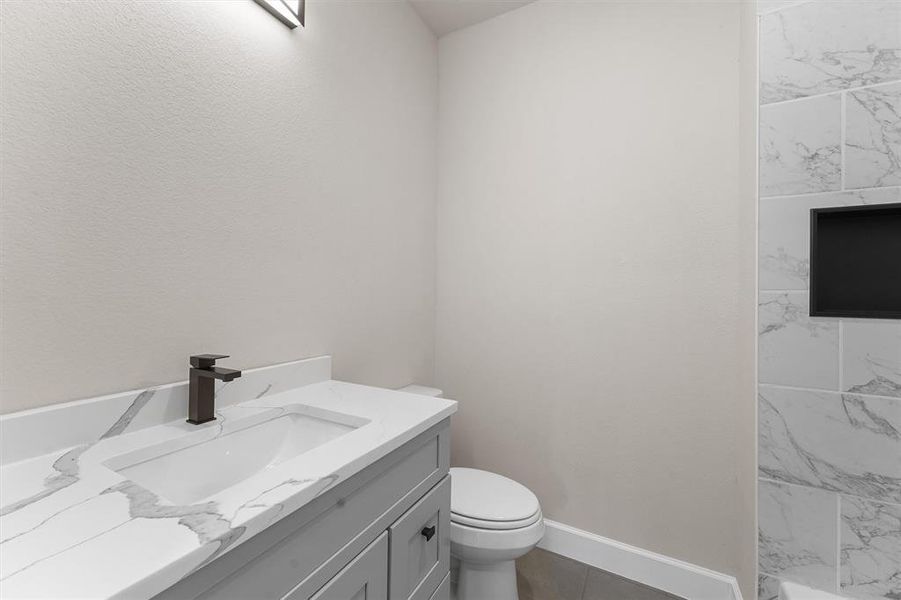 Modern bathroom featuring a marble countertop with integrated sink, sleek dark faucet, and a tiled shower area.