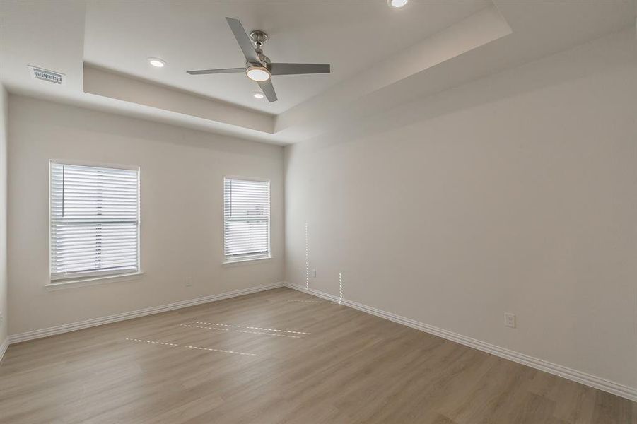 Empty room with a tray ceiling, light hardwood / wood-style flooring, and ceiling fan