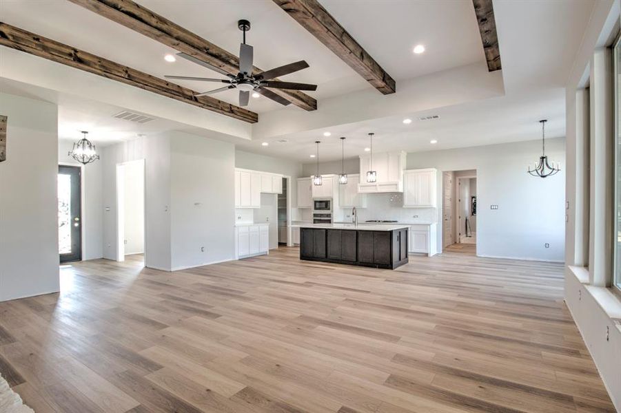 Unfurnished living room with beamed ceiling, sink, light hardwood / wood-style flooring, and ceiling fan with notable chandelier