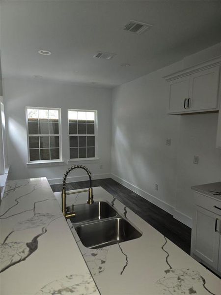 Kitchen featuring light stone counters, white cabinets, and sink