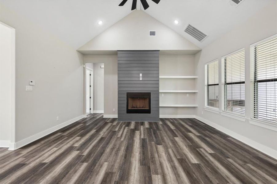 Unfurnished living room with built in shelves, a fireplace, dark hardwood / wood-style flooring, high vaulted ceiling, and ceiling fan