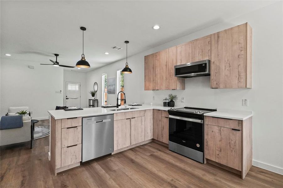 Kitchen with dark wood-type flooring, sink, hanging light fixtures, stainless steel appliances, and light brown cabinetry