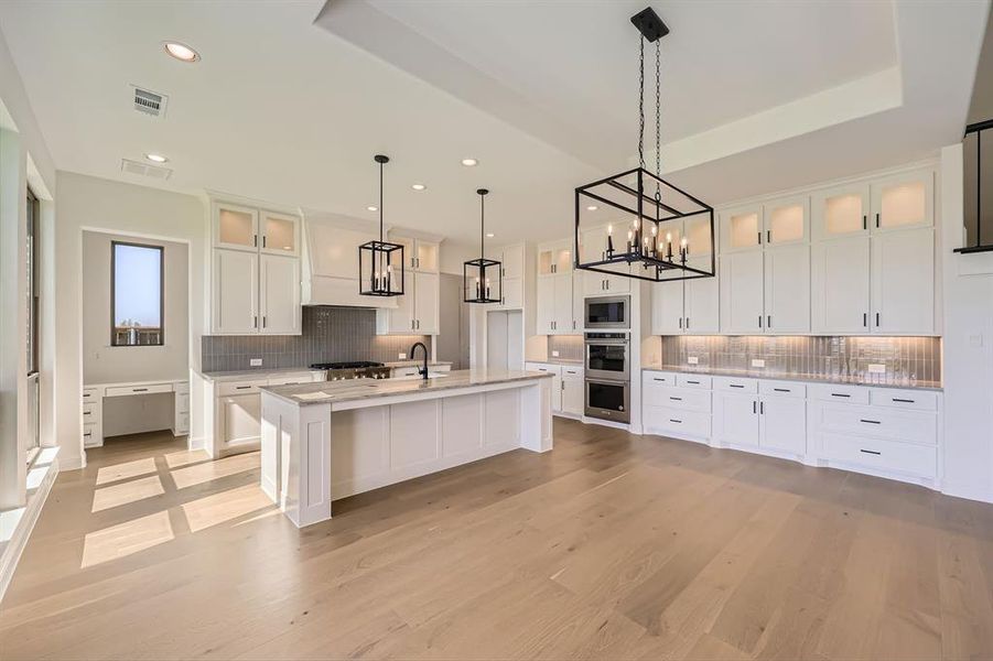 Kitchen featuring a center island with sink, decorative backsplash, light hardwood / wood-style flooring, white cabinetry, and appliances with stainless steel finishes