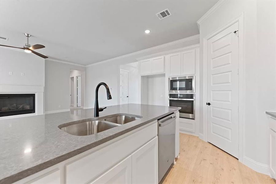 Kitchen with white cabinetry, ceiling fan, stainless steel appliances, light hardwood / wood-style floors, and sink