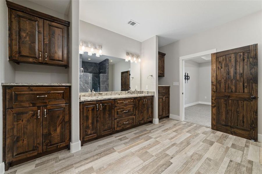 Flanking the expansive double sink vanity are extra cabinets and counter space, offering convenient storage options and enhancing the functionality of the bathroom. This setup not only maximizes organization but also ensures that both sides of the vanity are well-equipped for your daily routines, making it easy to keep essentials within reach while maintaining a neat and spacious environment.