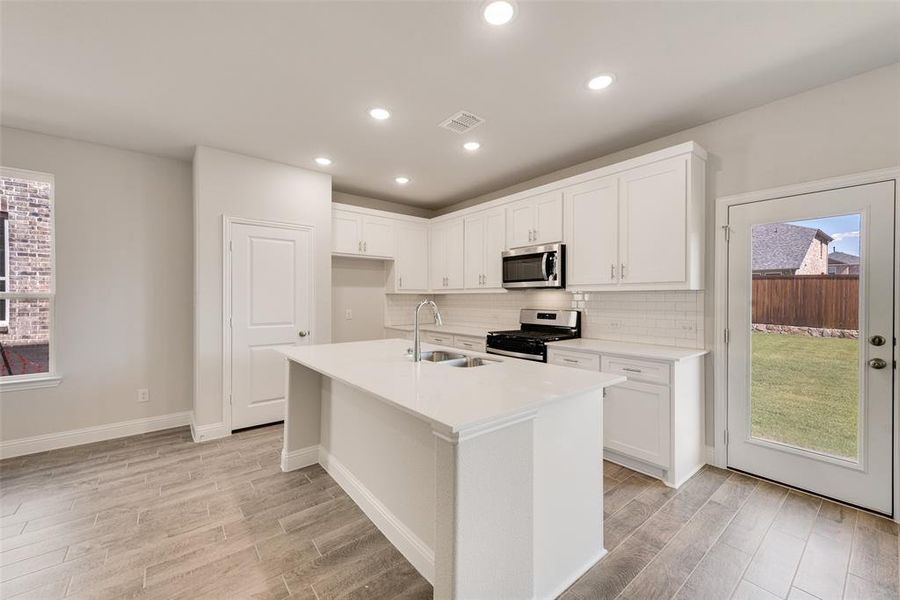 Kitchen featuring light wood-type flooring, sink, an island with sink, white cabinets, and appliances with stainless steel finishes