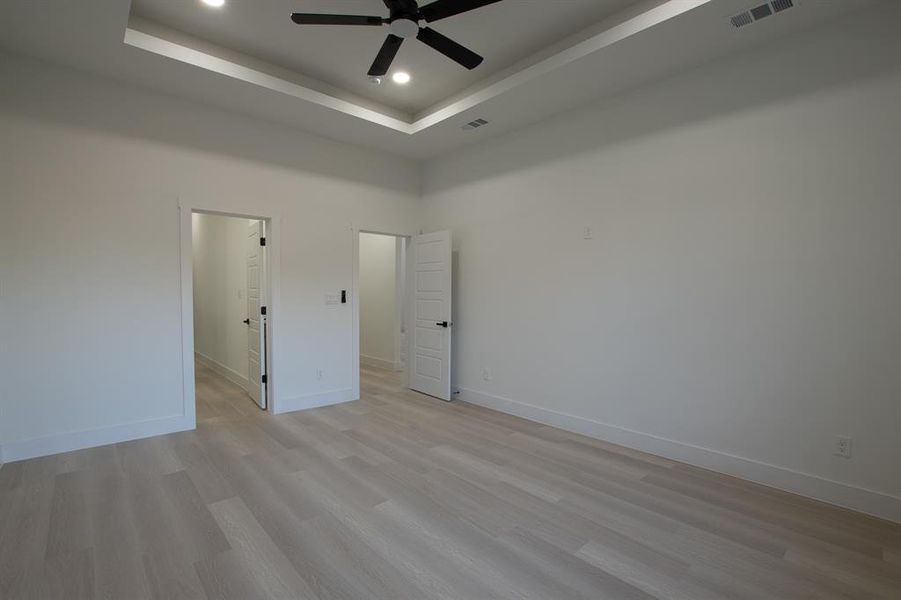 Unfurnished room with light wood-type flooring, ceiling fan, a high ceiling, and a tray ceiling