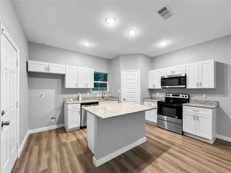 Kitchen with light stone counters, light hardwood / wood-style floors, white cabinetry, a center island, and appliances with stainless steel finishes
