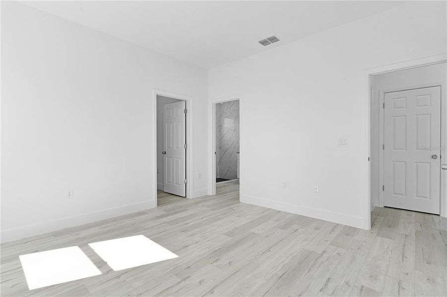 View from primary bedroom corner looking at walk-in closet door (left) and primary bath door (center), with bedroom doorway to the right