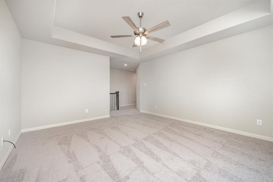 Unfurnished room featuring ceiling fan, light carpet, and a tray ceiling