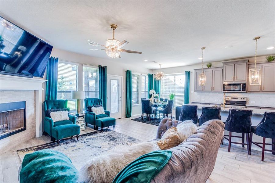 Living room with a wealth of natural light, ceiling fan, a tile fireplace, and light wood-type flooring