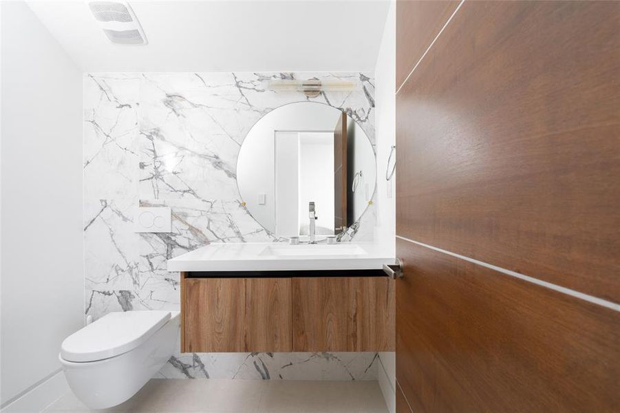 This elegant third-floor powder bath showcases a stunning stone feature wall with dramatic veining, adding a touch of luxury to the space. The sleek floating vanity, with a minimalist wood finish, provides ample storage for towels and toiletries.