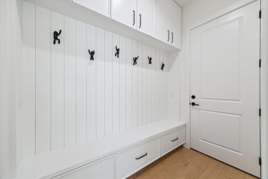 The mudroom (7’x 4’11”) features engineered white oak flooring and a built-in bench with drawers underneath. Pennygap wall detailing and sculptural clothing hooks add style, while recessed LED lighting enhances the functionality of the space. Convenient access to the garage completes this practical and elegant area.