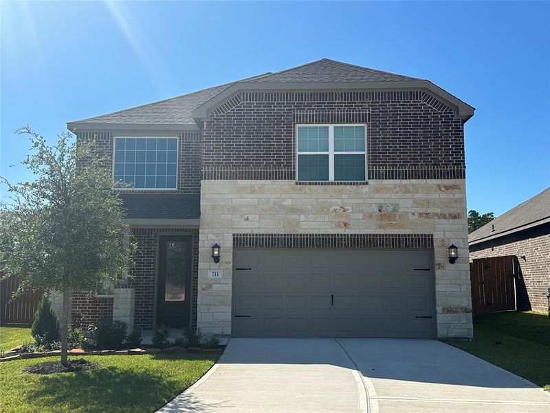 The Sequoia is a beautiful two-story home with a unique two-tone brick and stone design. The home has front yard landscaping and upgraded light fixtures on either side of the garage, with large windows for added curb appeal.