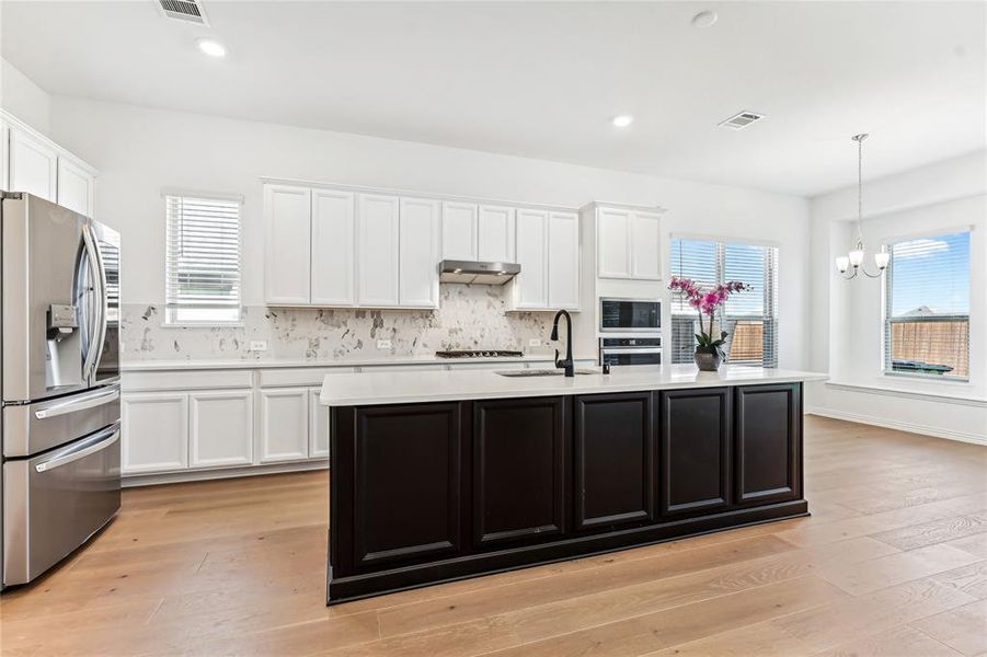 Kitchen featuring pendant lighting, appliances with stainless steel finishes, a chandelier, and light hardwood / wood-style flooring