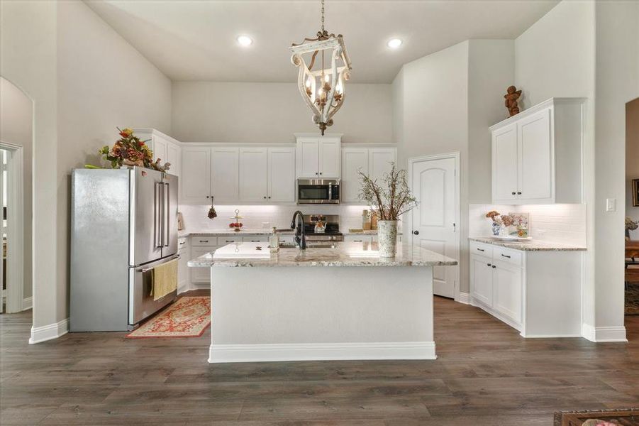 Kitchen featuring appliances with stainless steel finishes, decorative backsplash, a kitchen island with sink, dark wood-type flooring, and a towering ceiling
