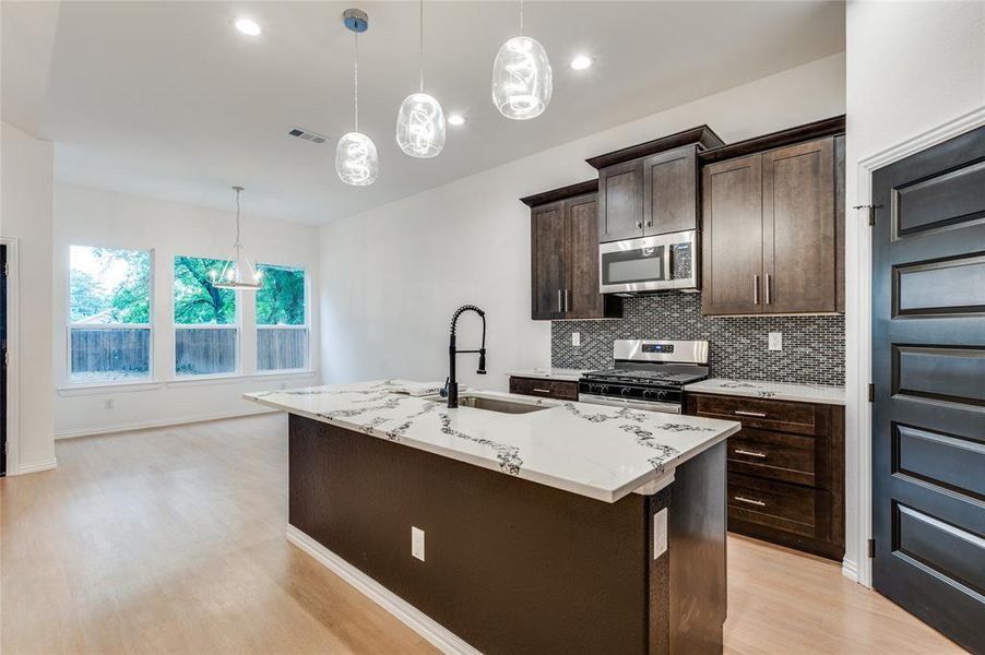 Kitchen featuring a kitchen island with sink, light wood-type flooring, stainless steel appliances, light stone counters, and sink