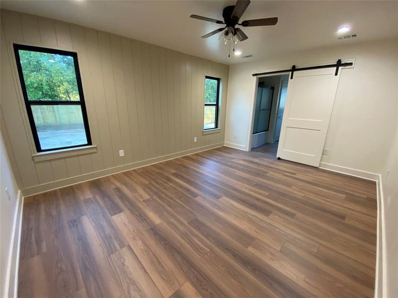 Unfurnished bedroom featuring ceiling fan, wooden walls, dark hardwood / wood-style floors, and a barn door