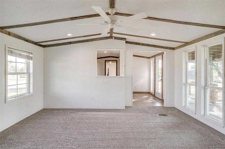 Carpeted spare room with a healthy amount of sunlight, ceiling fan, and vaulted ceiling with beams