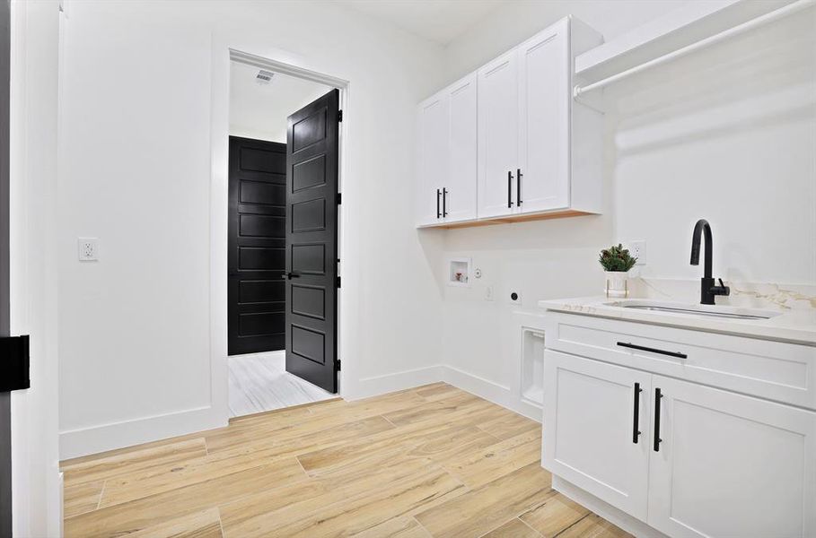 Clothes washing area featuring electric dryer hookup, cabinets, sink, hookup for a washing machine, and light hardwood / wood-style floors