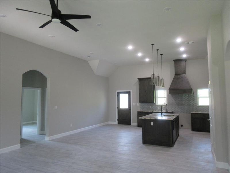 Kitchen featuring custom range hood, ceiling fan, decorative backsplash, pendant lighting, and a center island with sink