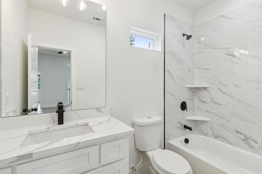 Full bathroom with vanity with extensive cabinet space, toilet, and tiled shower / bath combo