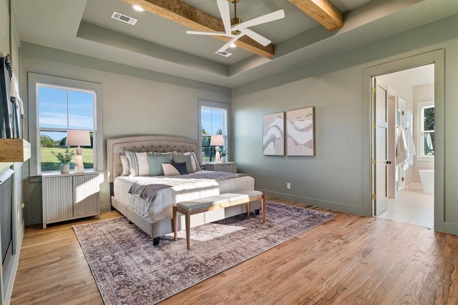 Bedroom with light hardwood / wood-style floors, ceiling fan, a tray ceiling, beamed ceiling, and ensuite bath