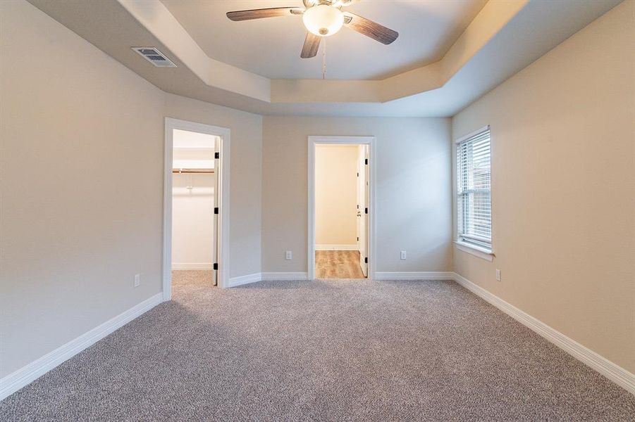 Bedroom with a tray ceiling, a walk in closet, light carpet, and ceiling fan