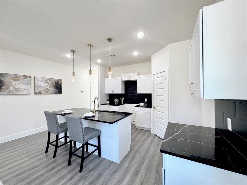 Kitchen featuring light hardwood / wood-style floors, white cabinets, decorative light fixtures, a center island with sink, and sink