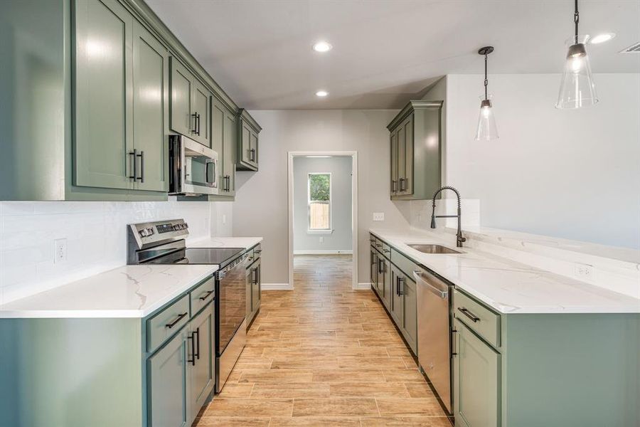 Kitchen with green cabinetry, pendant lighting, stainless steel appliances, and light hardwood / wood-style flooring