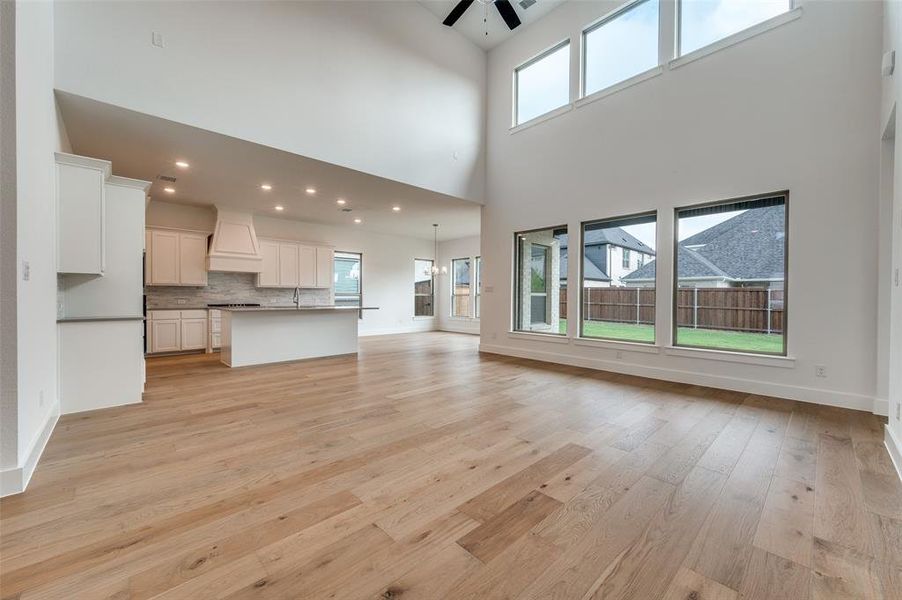 Unfurnished living room with sink, light hardwood / wood-style floors, a towering ceiling, and ceiling fan