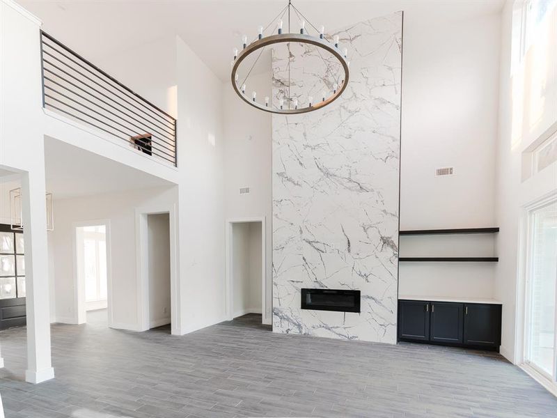 Unfurnished living room with a chandelier, a high end fireplace, a high ceiling, and light hardwood / wood-style flooring