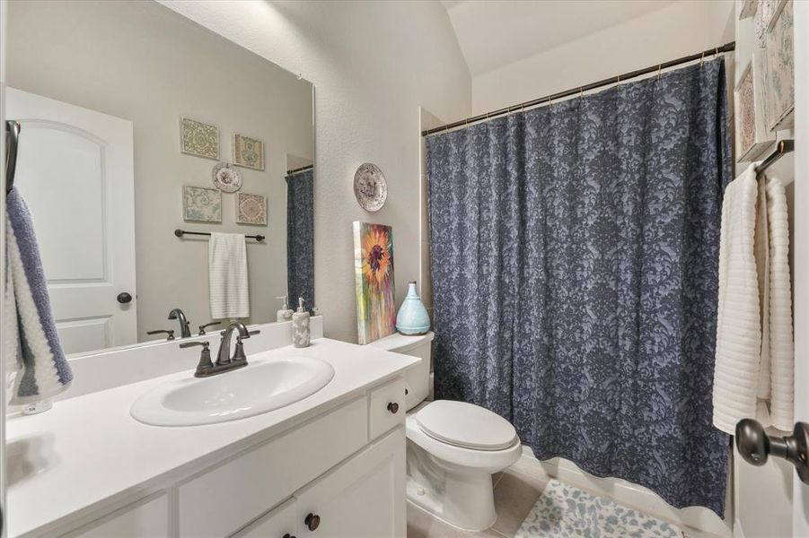 Bathroom featuring tile patterned floors, toilet, vanity, and vaulted ceiling