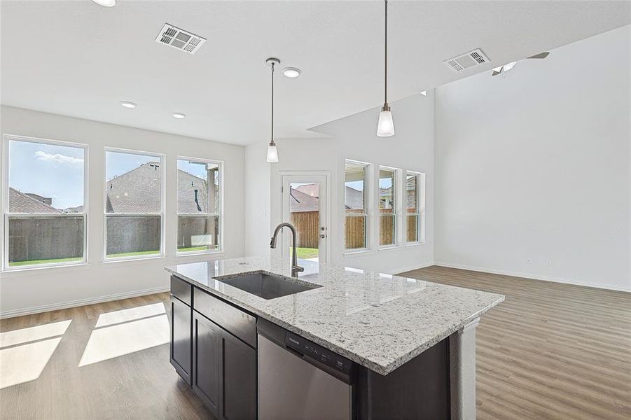 Kitchen with dishwasher, a kitchen island with sink, wood-type flooring, sink, and decorative light fixtures