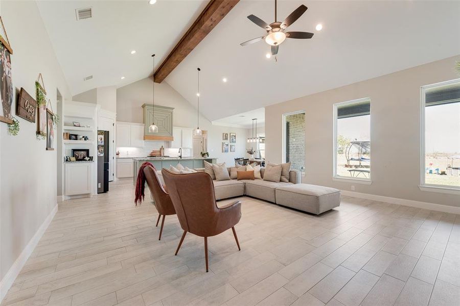 Living room with ceiling fan, beamed ceiling, light wood-type flooring, and high vaulted ceiling