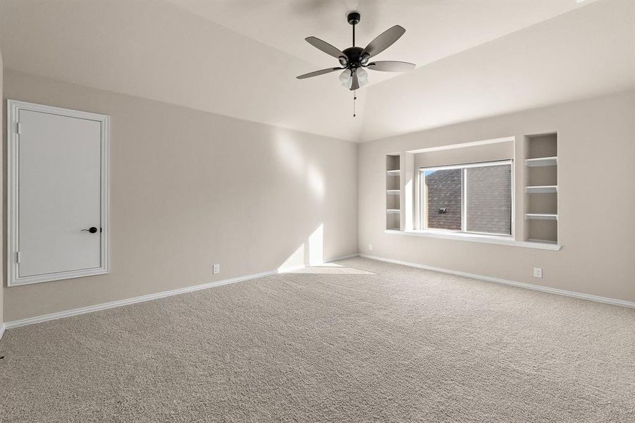 Carpeted empty room with lofted ceiling, ceiling fan, and built in shelves