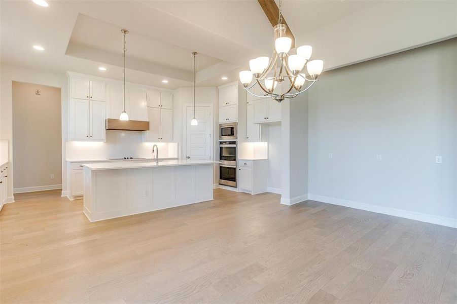 Kitchen featuring a notable chandelier, light hardwood / wood-style flooring, white cabinets, and a raised ceiling