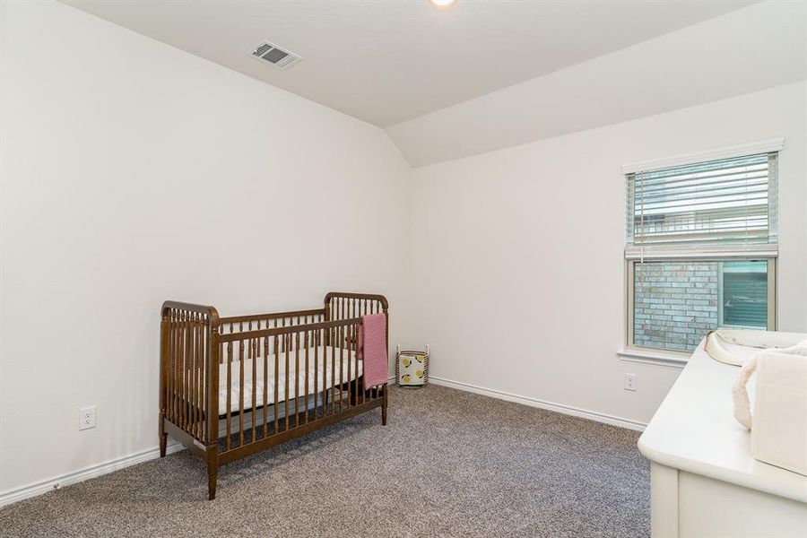 Bedroom featuring lofted ceiling, carpet flooring, and a crib