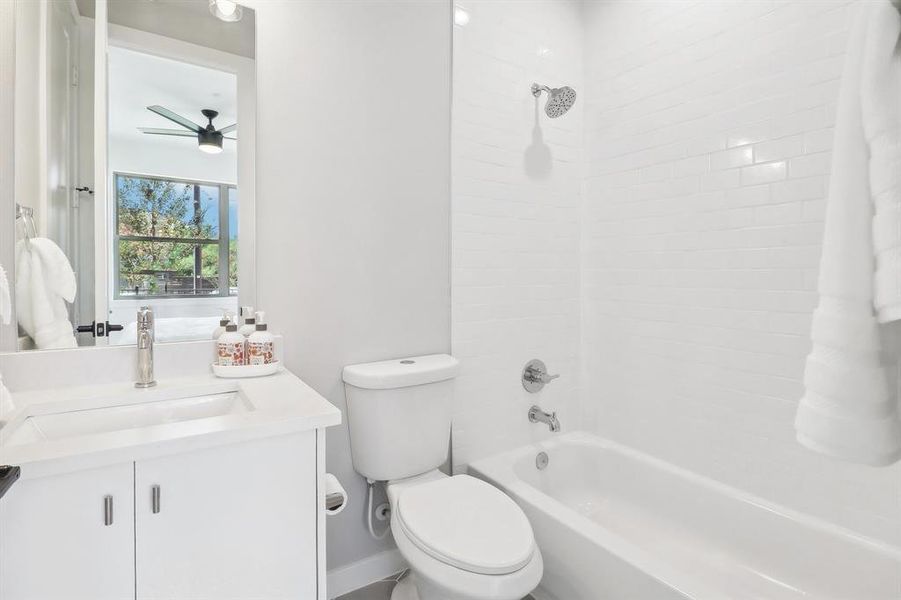 Full bathroom with tiled shower / bath combo, vanity, ceiling fan, and toilet