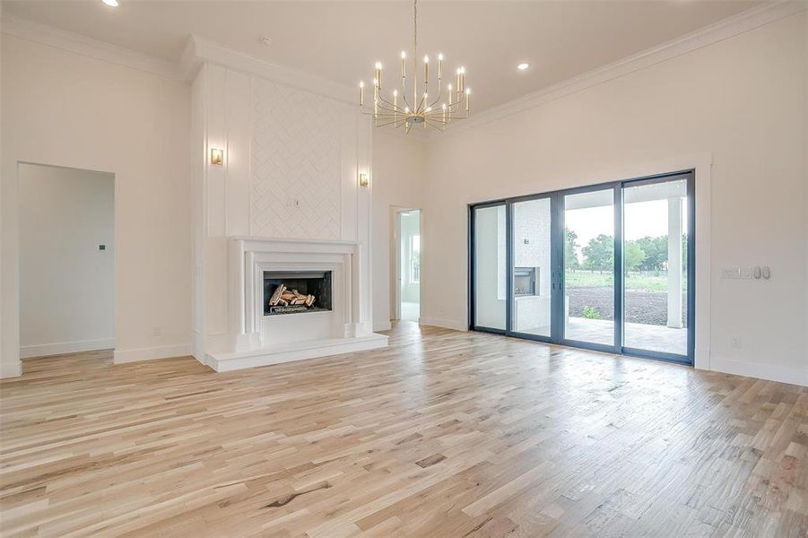 Unfurnished living room featuring an inviting chandelier, a high ceiling, light wood-type flooring, and ornamental molding